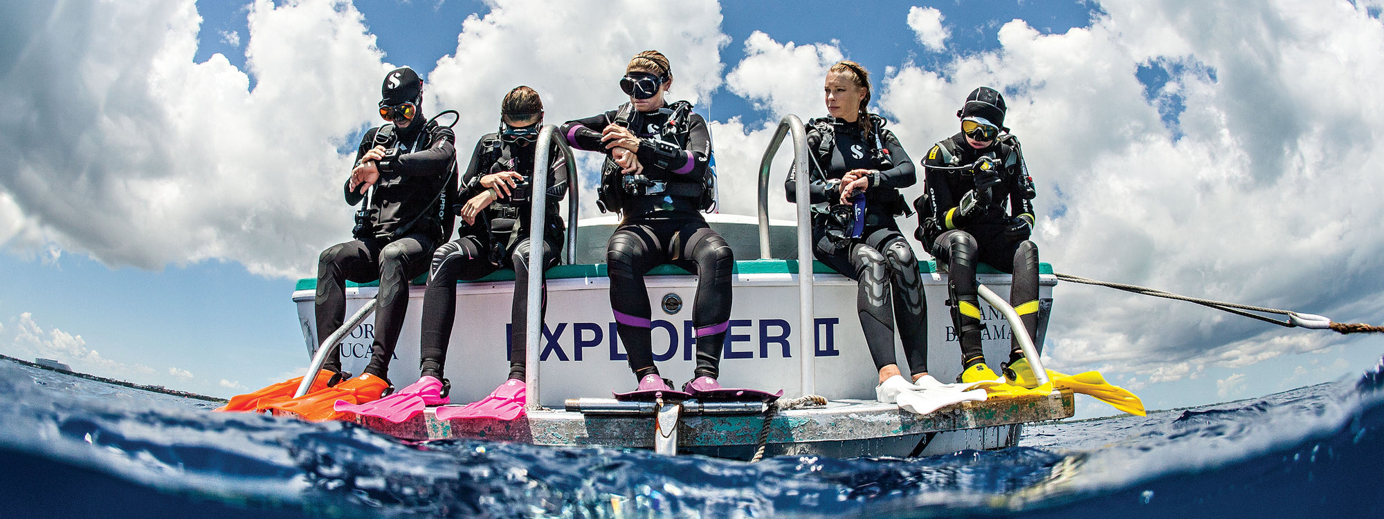 five scuba divers sitting on the back of a dive boat about to enter the water for their dive